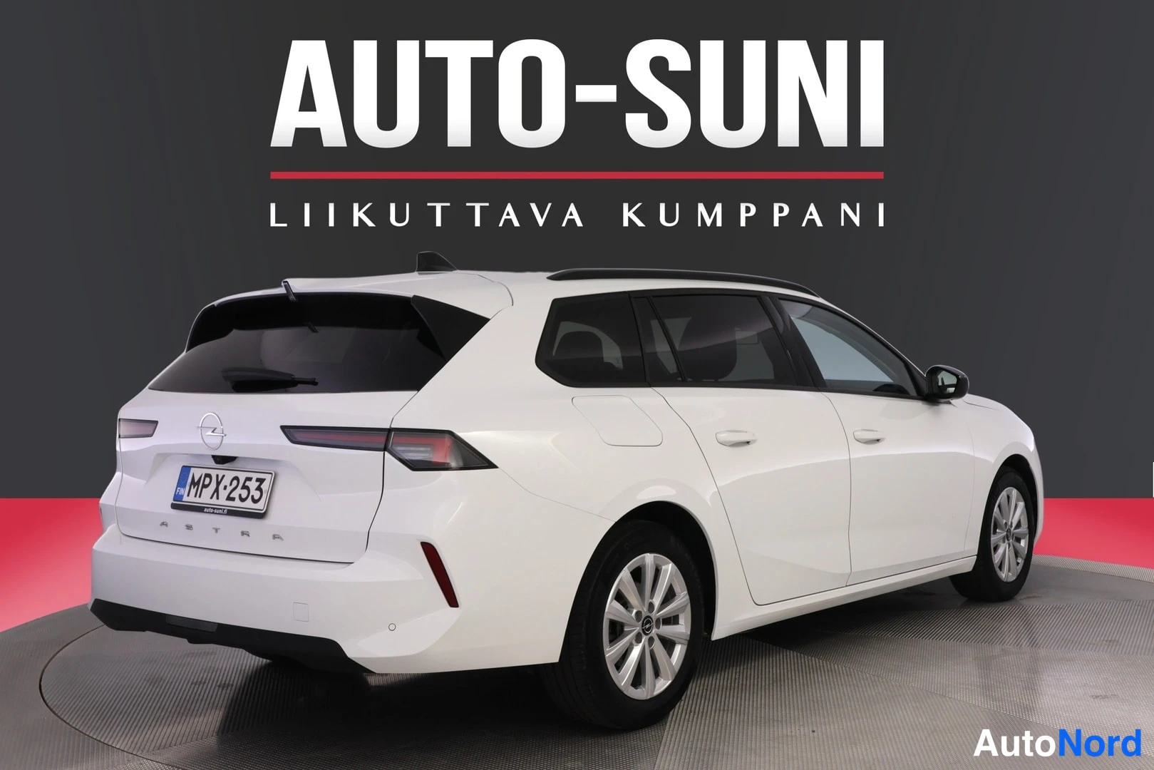 Takaviisto: Valkoinen farmariauto takakulmasta vasemmalta kuvattuna studiossa. Näkyvät takavalot, takaluukku Opel-tunnuksella, rekisteri, Astra-teksti ja auton oikea sivu.