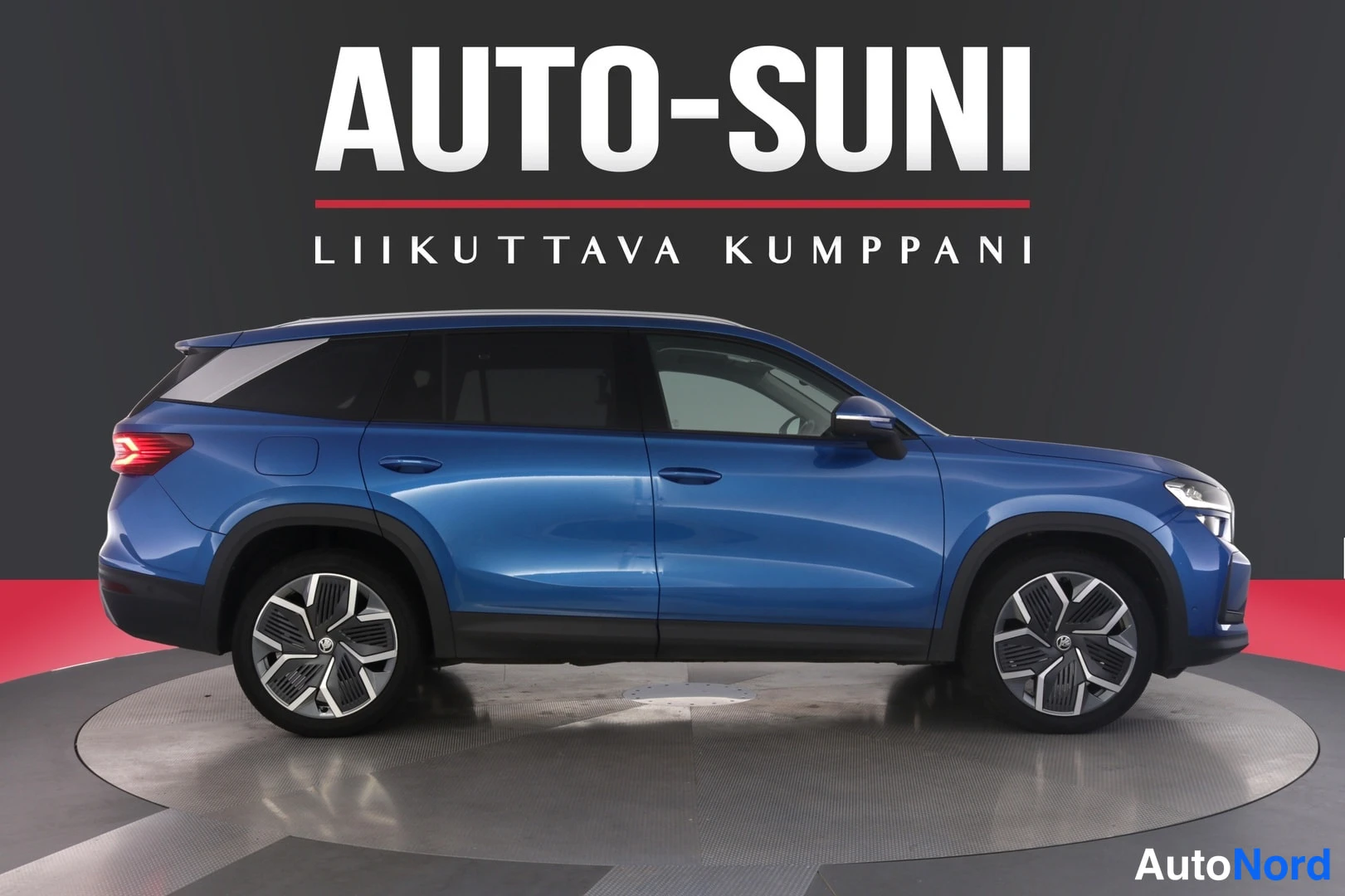 Sivulta: Sininen tilavaauto sivulta kuvattuna studiossa, taustalla Auto-Suni-mainoskuvio.