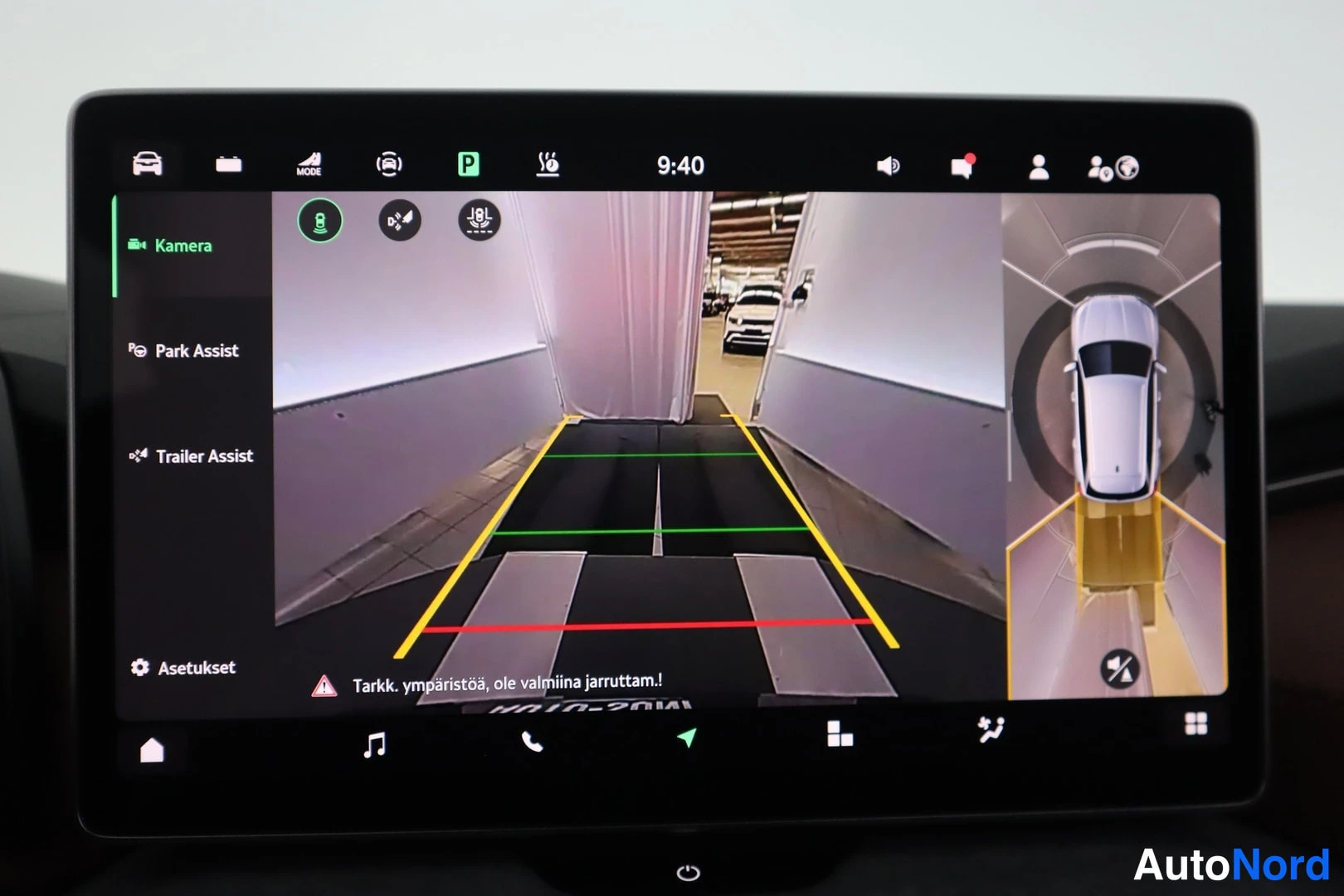 Muu: Auton infotainment-näyttö, jossa parkkikameran kuva ohjeviivoineen ja sivupalkissa valinnat Kamera, Park Assist, Trailer Assist ja Asetukset.