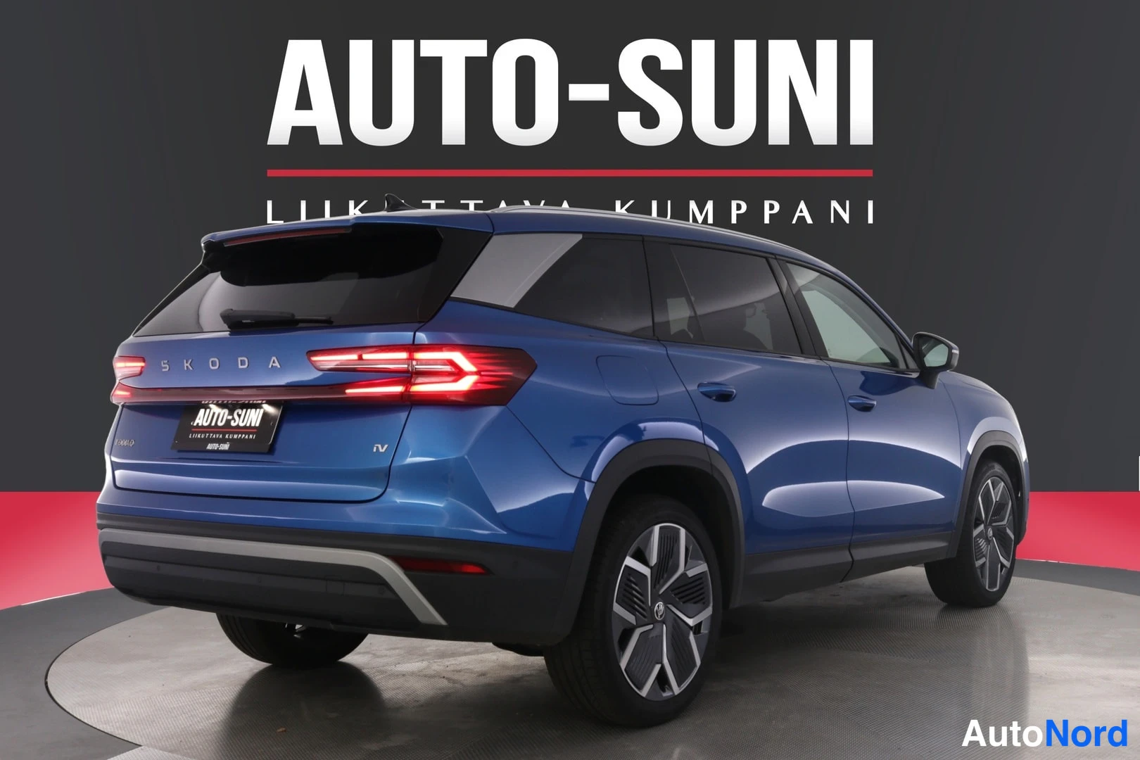 Takaviisto: Sininen tilavaauto takaa vasemmalta kuvattuna, taaksevalot syttyneinä, taustalla Auto-Suni-logo.