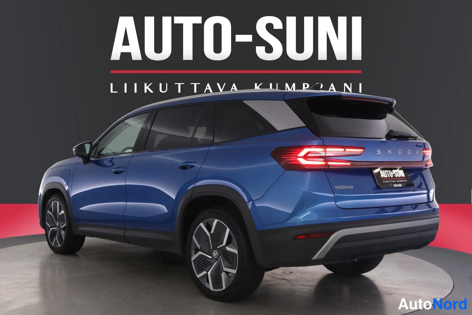 Takaviisto: Sininen tilavaauto takaa oikealta kuvattuna studiossa, taustalla Auto-Suni-mainosteksti.