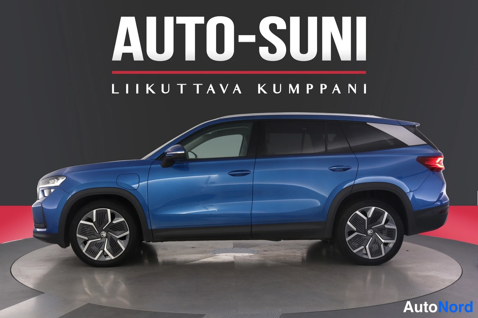 Sivulta: Sininen Skoda Kodiaq -maasturi sivulta kuvattuna studio­taustaa vasten, AUTO-SUNI-logo kuvan yläosassa.