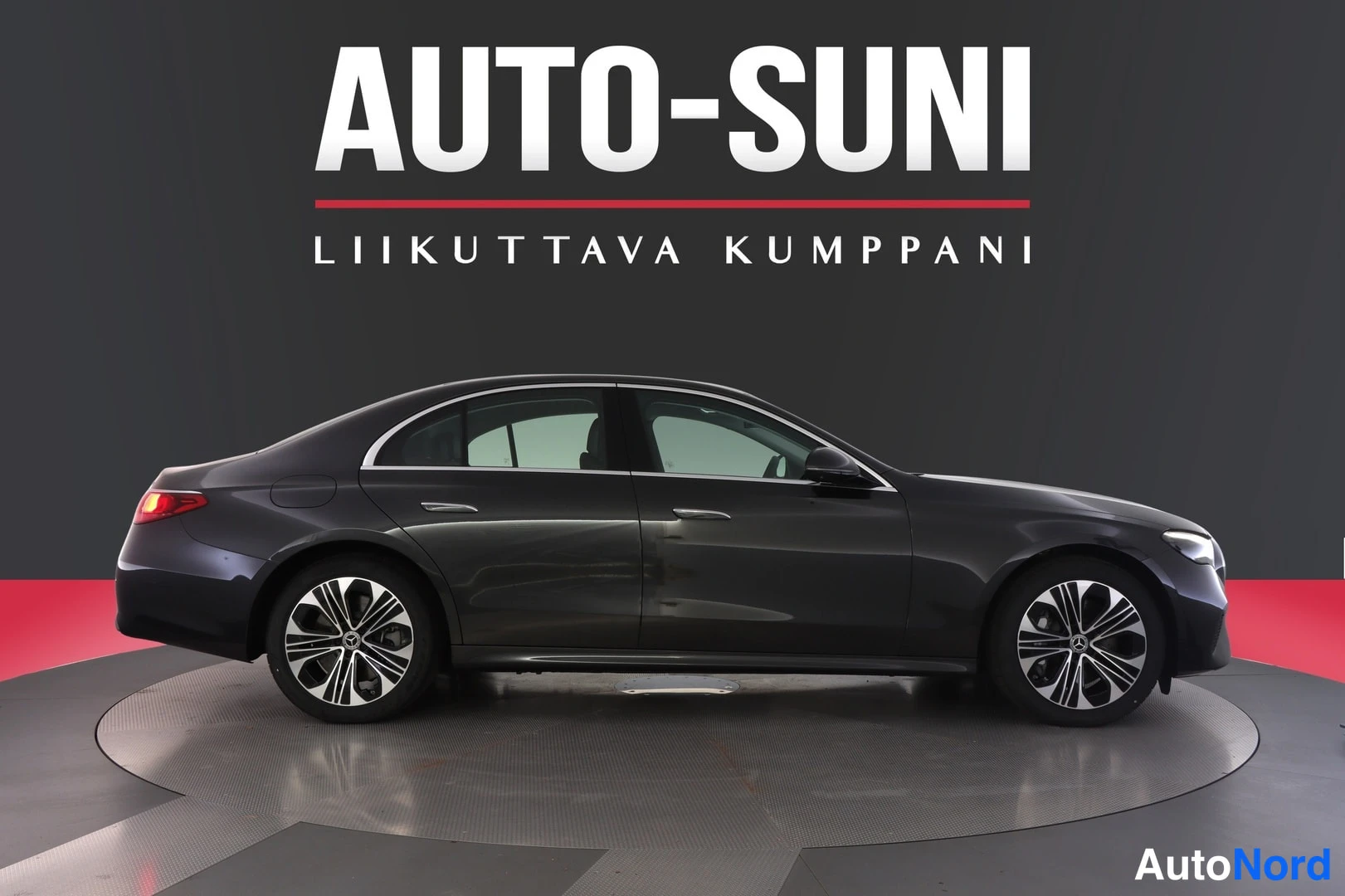 Sivulta: Tummanharmaa Mercedes-Benz E-sarjan sedan sivulta nähtynä, kokonaisauto näkyvissä studiotaustaa vasten.