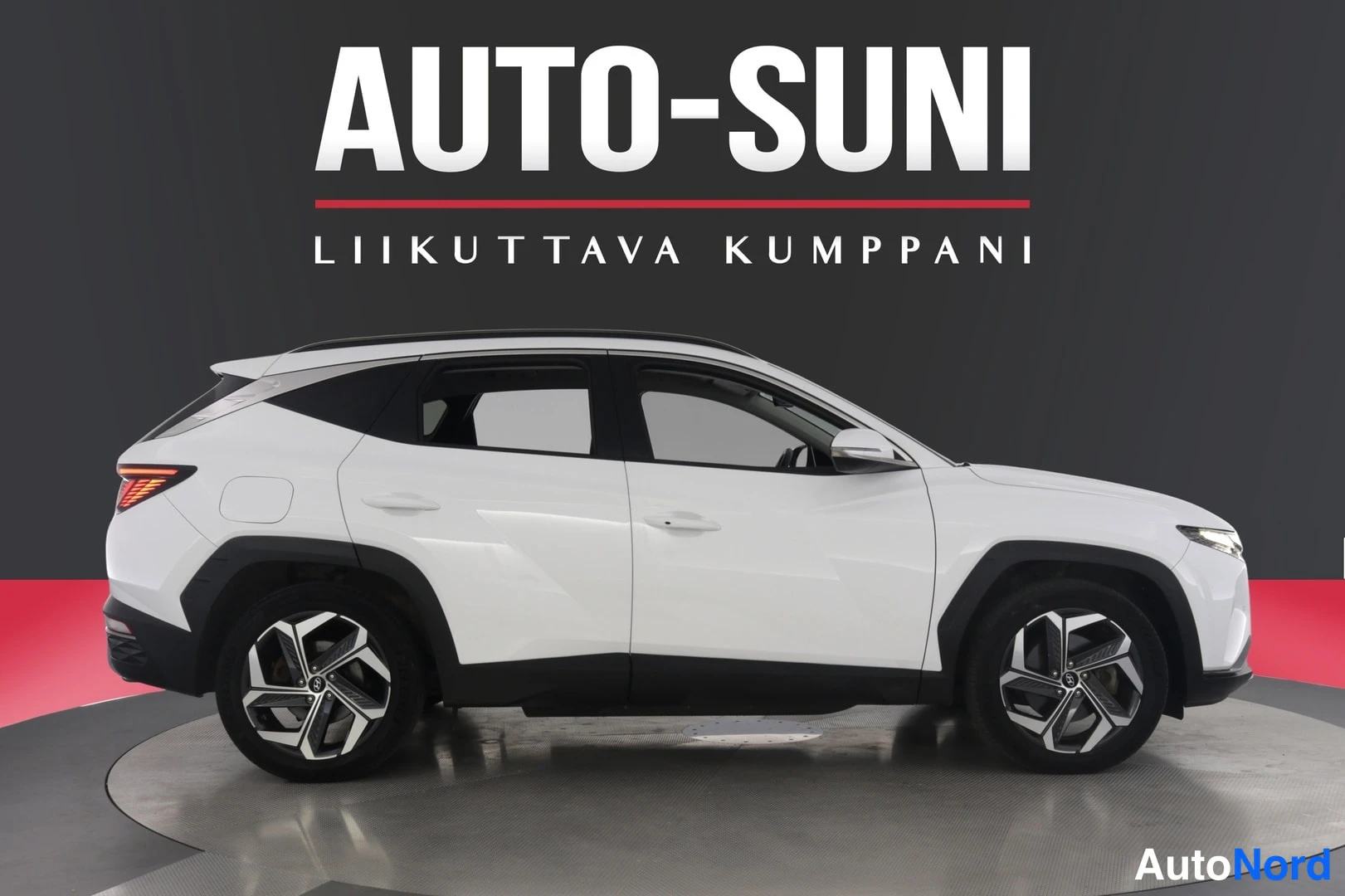 Sivulta: Valkoinen Hyundai Tucson sivulta kuvattuna studiotaustaa vasten.