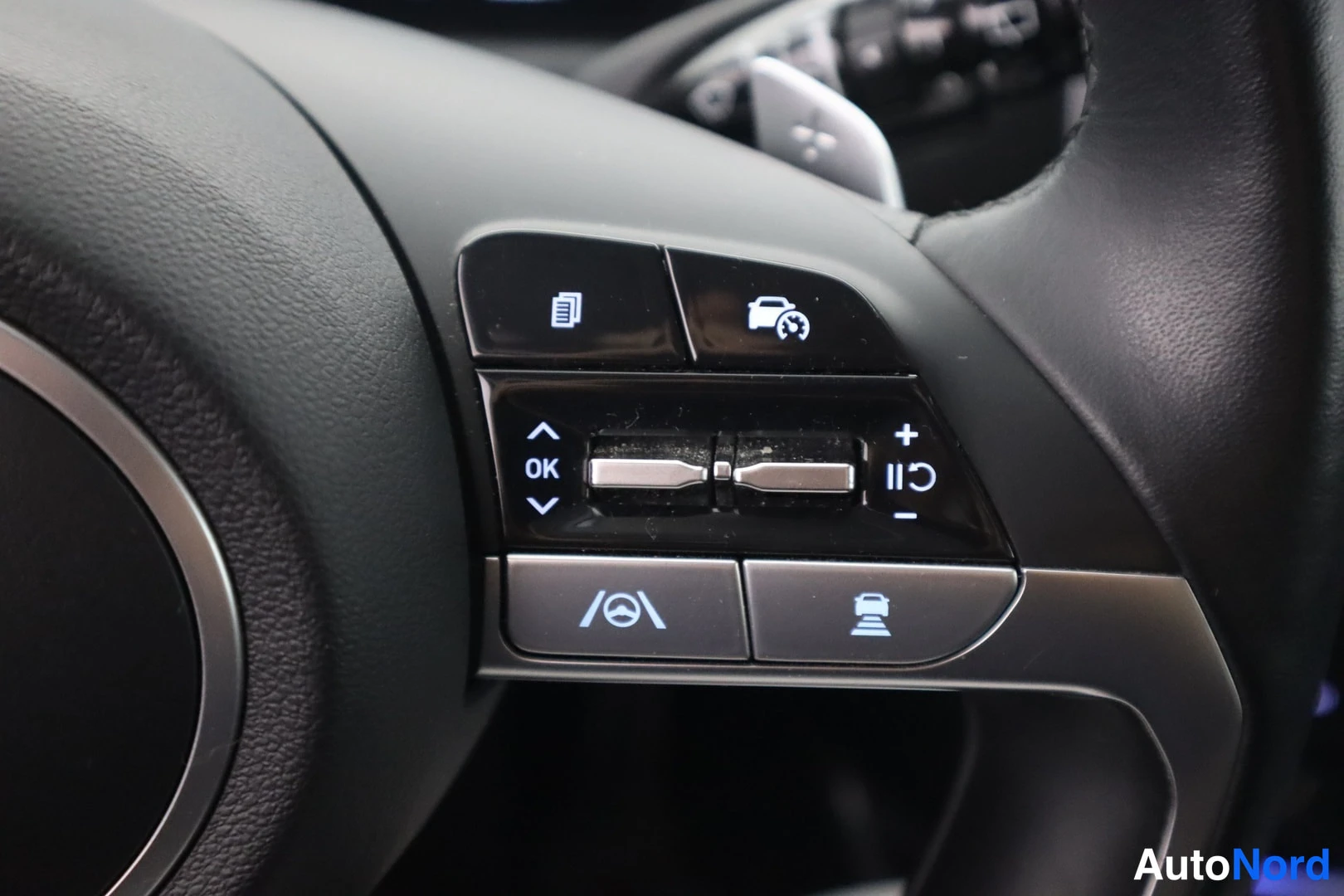 Muu: Hyundai Tucsonin ratin oikean puolen napipaneeli lähikuvassa: OK- ja nuolinapit, plus/miinus ja II-merkinnät sekä nopeusrajoittimen ja ajoneuvon symbolit.