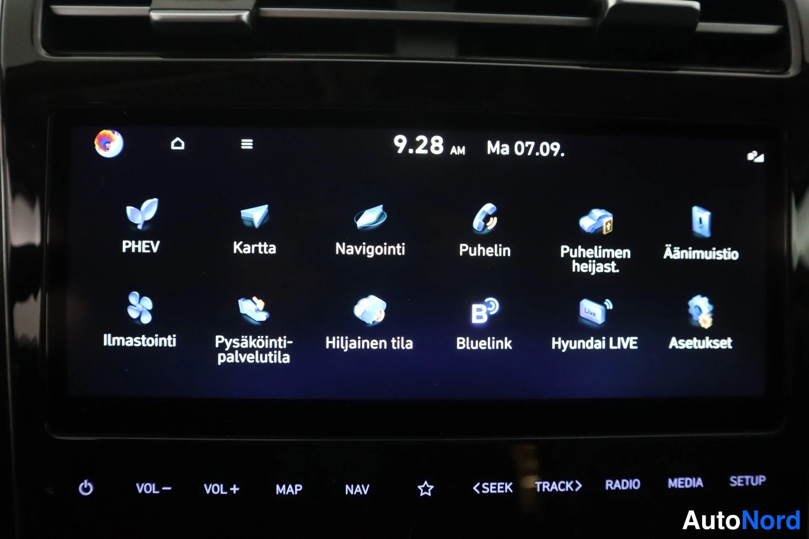 Yksityiskohta: Hyundain infotainment-järjestelmän päävalikko, jossa sovelluksia kuten PHEV, Kartta, Navigointi, Puhelin, Puhelimen heijastus, Äänimuistio, Ilmastointi, Pysäköi
