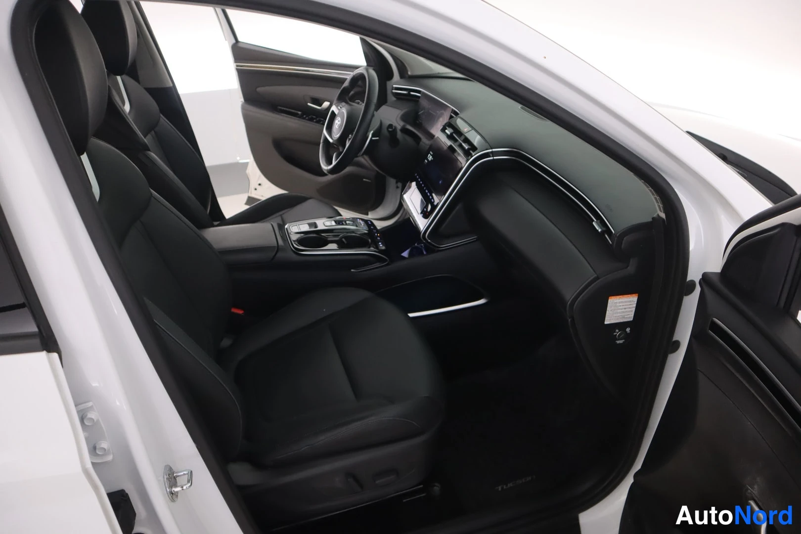 Muu: Hyundai Tucsonin etuistuimet ja hallintapaneeli avatusta ovasta katsottuna; matkustamo on mustaa ja korin runko valkoinen.