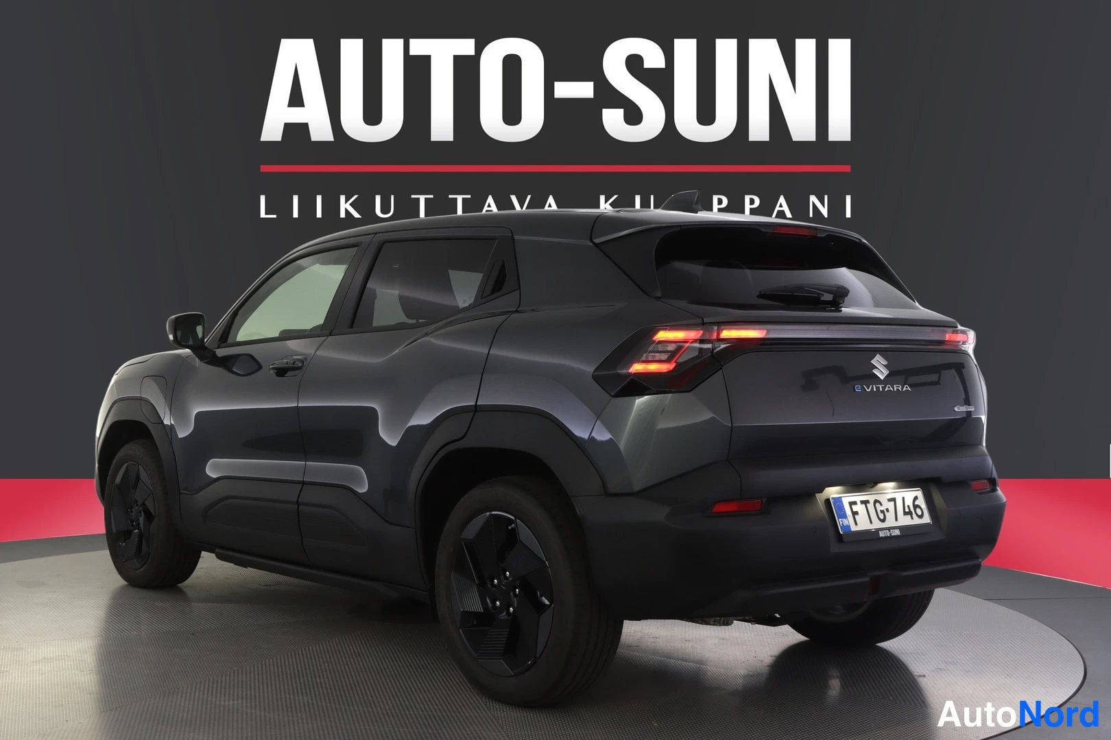 Takaviisto: Tummanharmaa henkilöauto takaviistosta toisesta kulmasta, rekisteritunnus, takaluukussa e VITARA -teksti.
