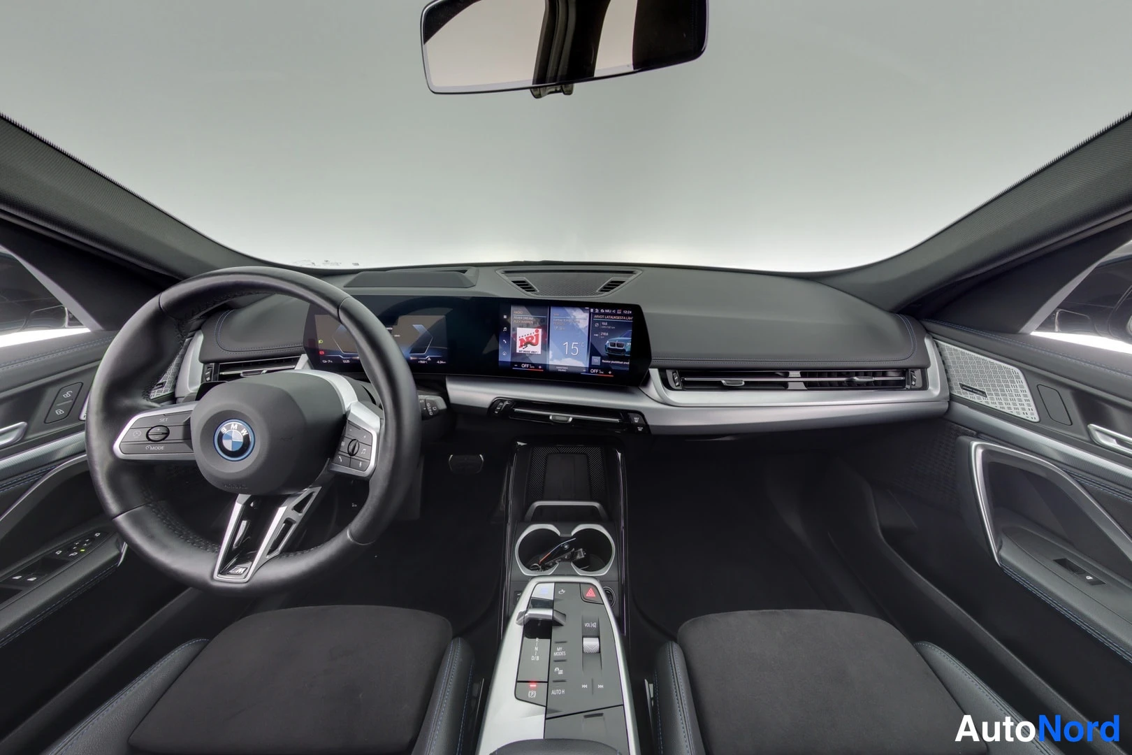 Muu: Auton ohjaamo etummaisesta paikasta: ohjauspyörä BMW-merkillä, laaja näyttö, keskiö Console ja vaihtajan säätimet.