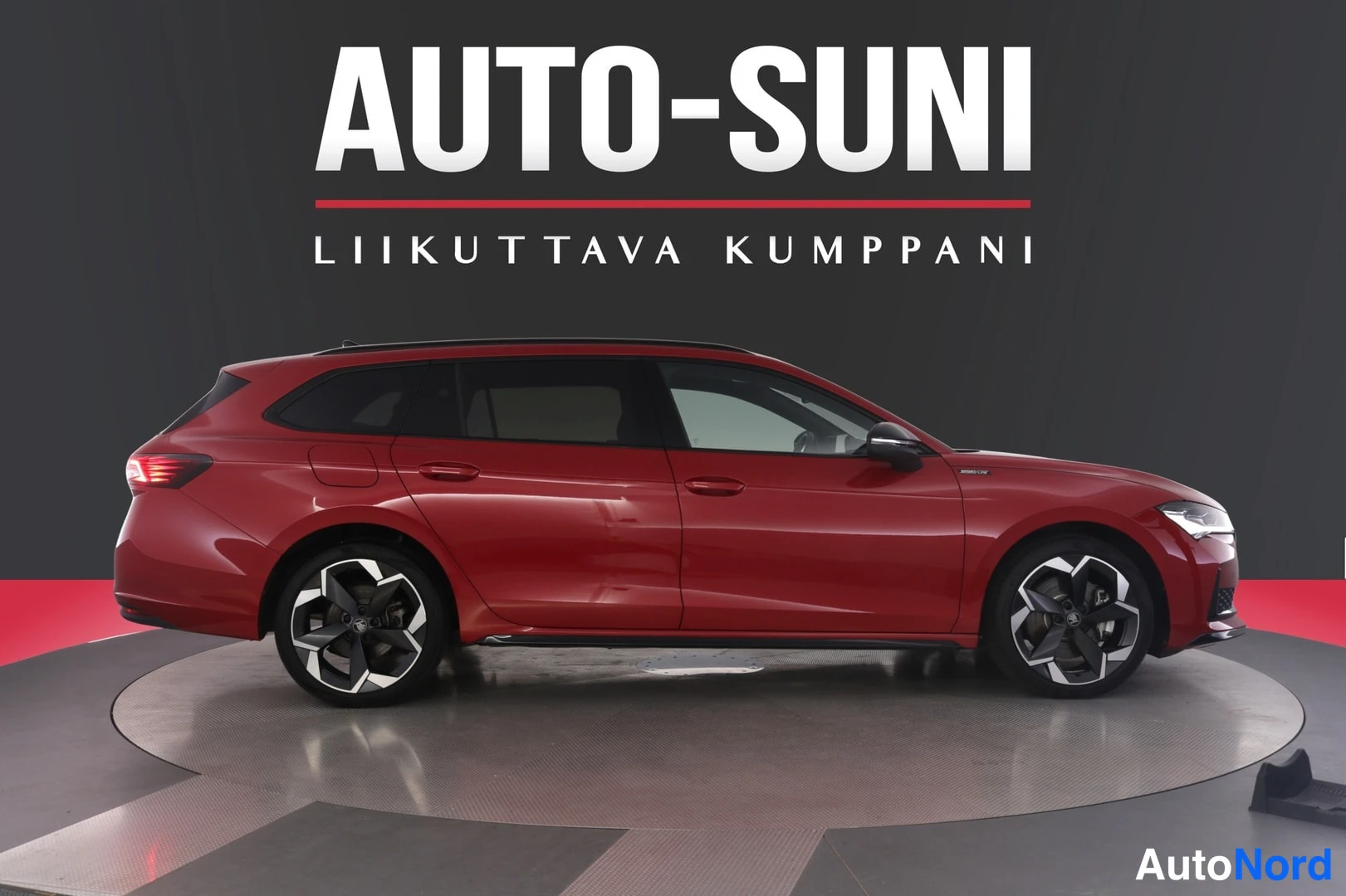 Etuviisto, nokka oikealle: Punainen farmariauto sivusuunnassa studiossa, kylki ja keulan kärki näkyvät oikealle.
