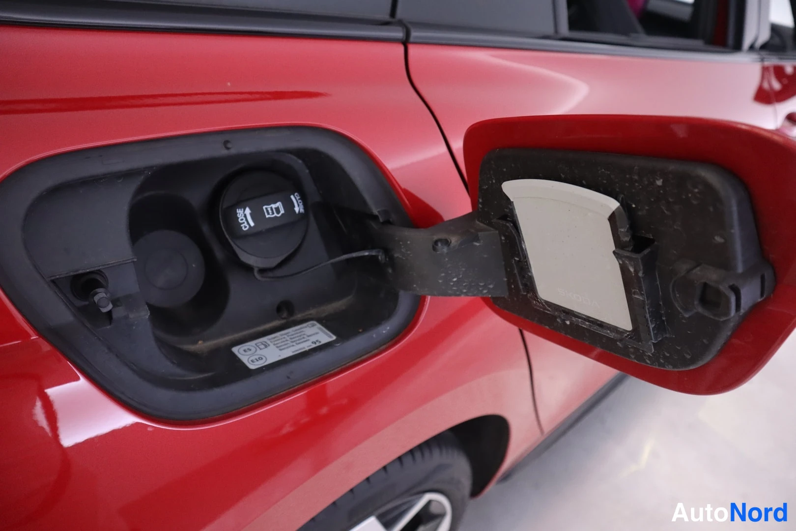Yksityiskohta: Punaisen auton auki avattu polttoainesuuttimeen vievä täyttöluukku, jossa musta E85-merkitty tankkikorkki ja E5-merkitty tarralusikka kannen sisäpuolella.