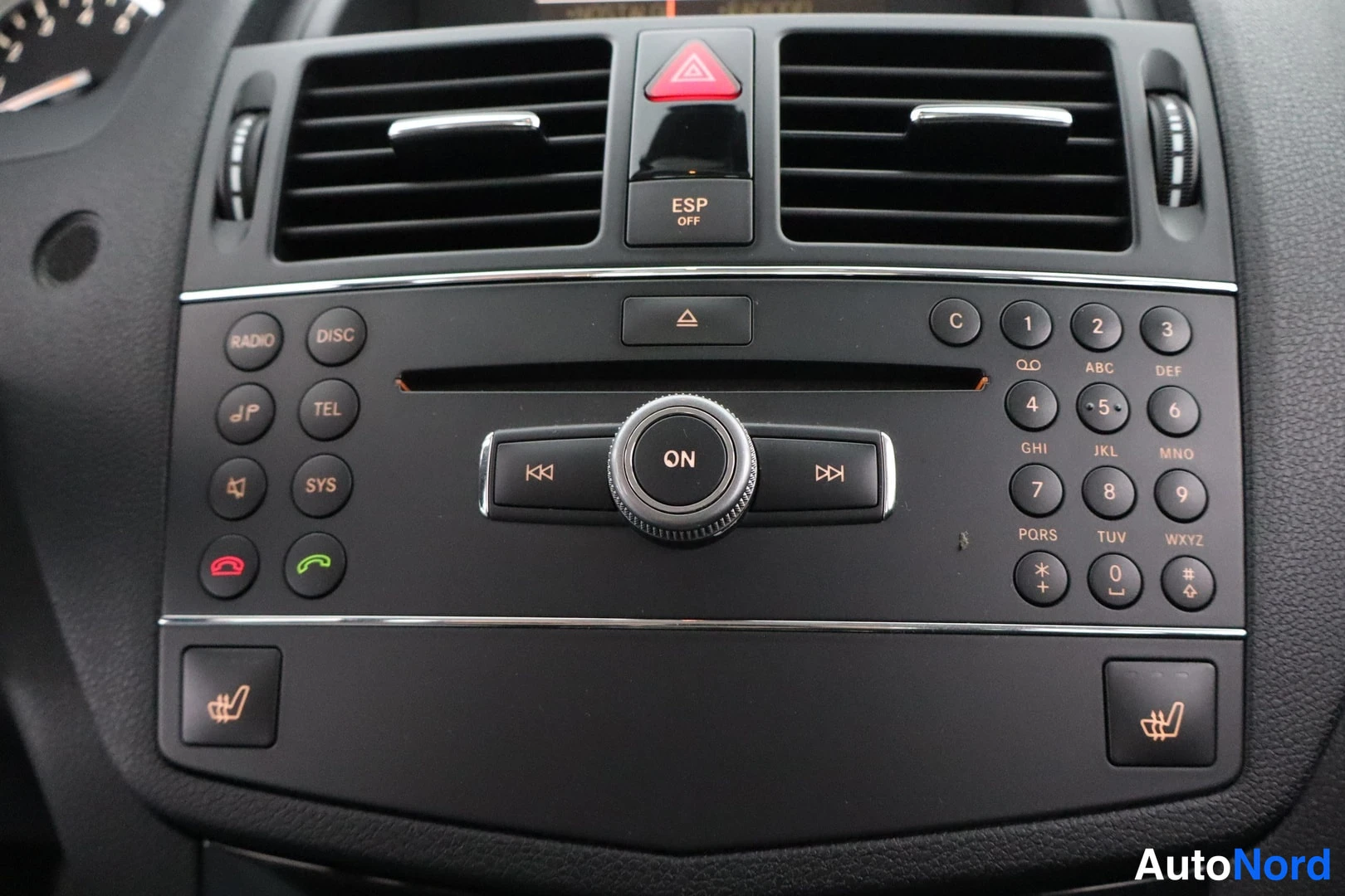 Edestä: Mercedes-Benzin keskikonsoli: ON-säädin, numeronäppäimistö, RADIO-, DISC-, TEL- ja SYS-painikkeet, ESP OFF-kytkin sekä istuimenlämmityspainikkeet.