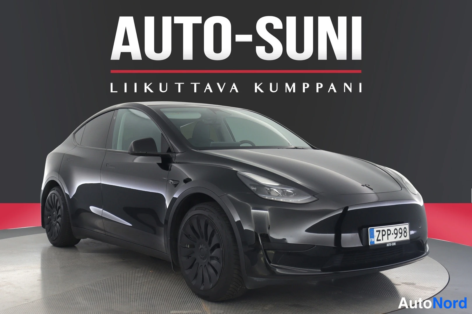 Etuviisto, nokka oikealle: Musta Tesla Model Y -henkilöauto etuosto-kulmakuvassa Auto-Suni-näyttämöllä, rekisteritunnukseltaan.