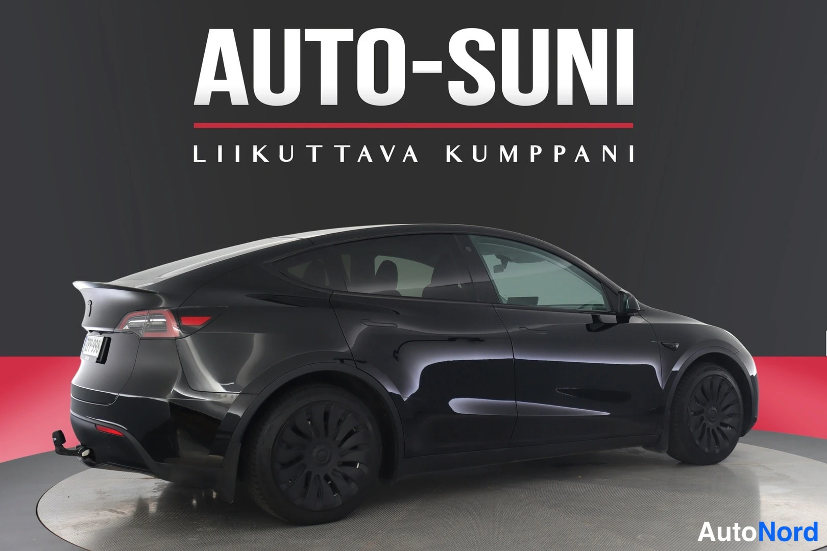 Takaviisto: Mustan Tesla Model Y -auton takaosto-kulmakuva sivulta, rekisteritunnus peittyneenä, takapuskuri ja heila nähtävissä.