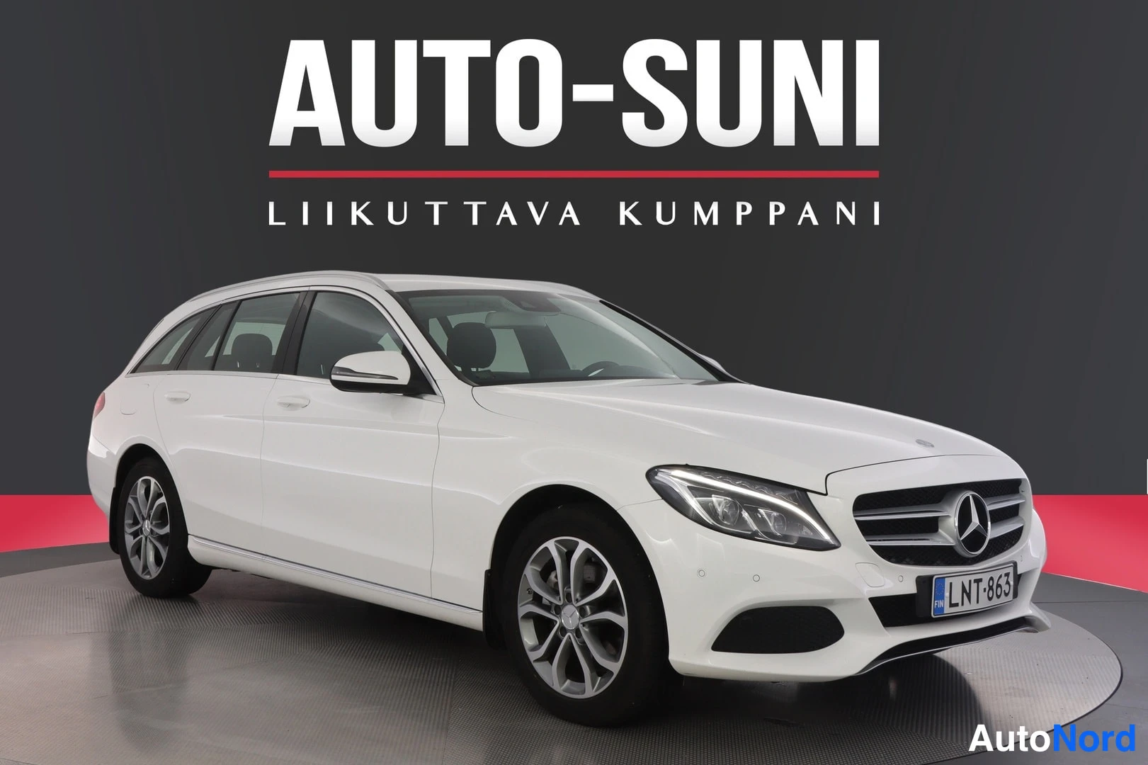 Etuviisto, nokka oikealle: Valkoinen Mercedes-Benz C farmari, etukolmisivukuva oikealta, rekisteritunnus, näyttelytilassa tumma tausta.