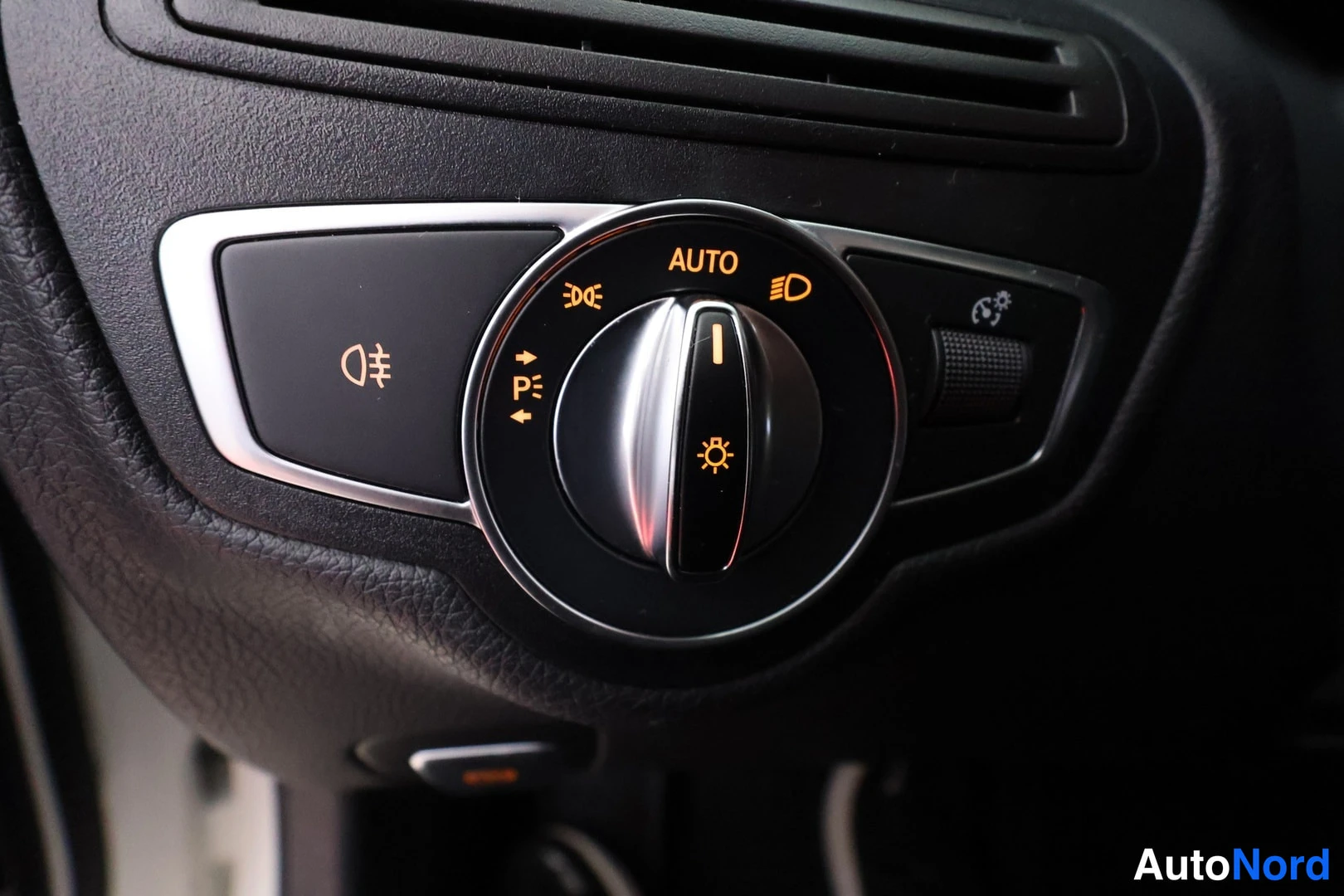 Yksityiskohta: Mercedes-Benzin sisätiloissa oleva pyöreä ajovalokytkin, jonka merkit ovat valaistu: AUTO-teksti ja suuntavalo-, seisontavalo- ja kylkivalkosymbolit.