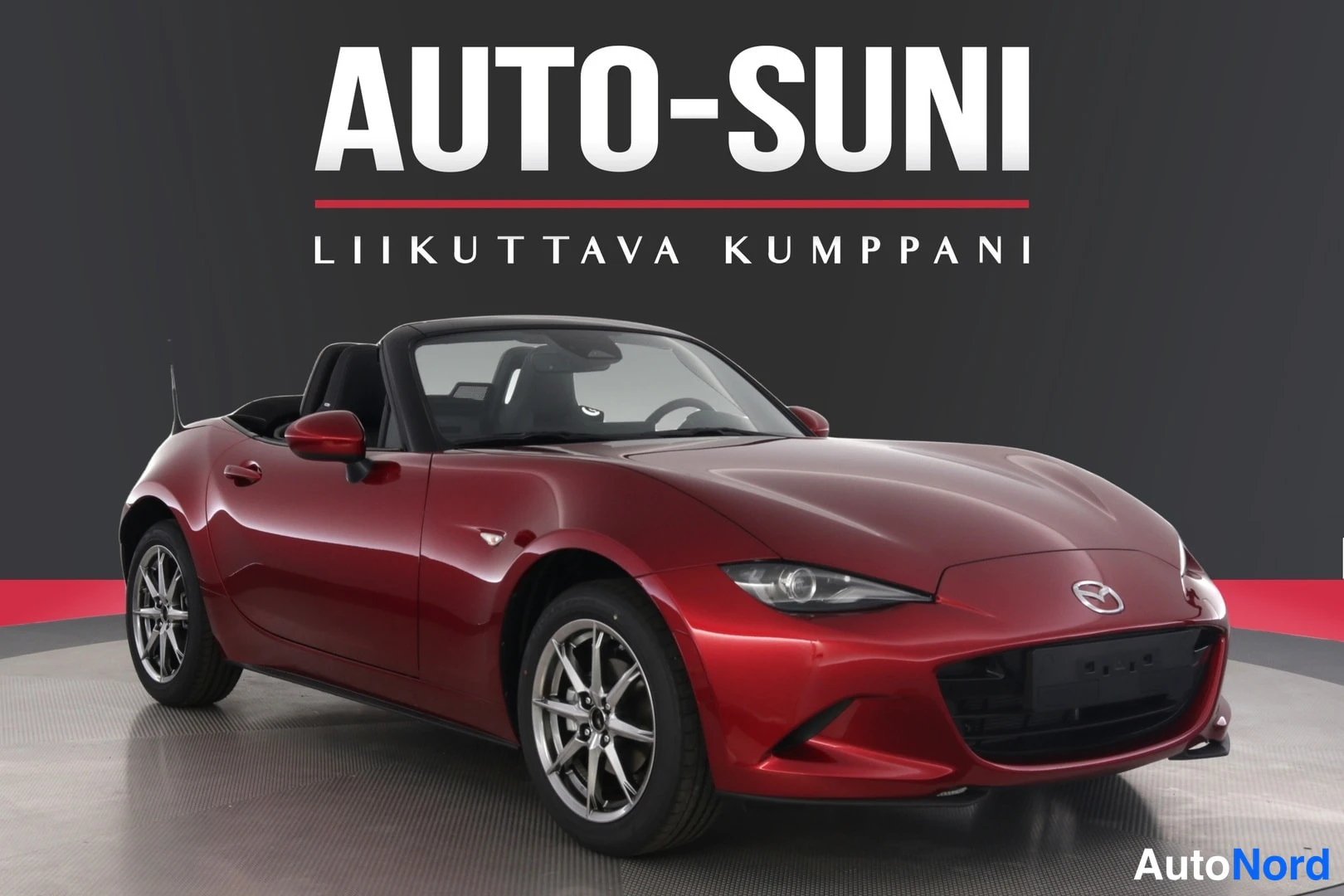 Etuviisto, nokka oikealle: Punainen avoin kaksipaikkainen urheiluauto kuvattu etuviistosta oikealta; tumma kangaskatto alas taitettuna, hopeat kevytmetallivanteet ja A-Sunnin maino