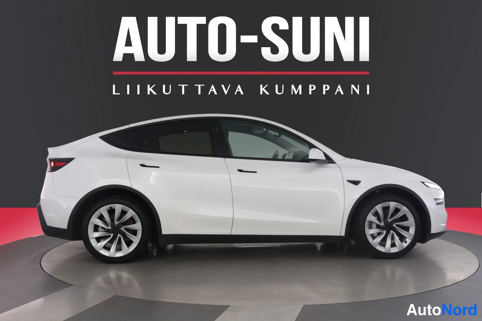 Sivulta: Valkoinen Tesla Model Y sivulta kuvattuna autosalin mustalla taustalla.