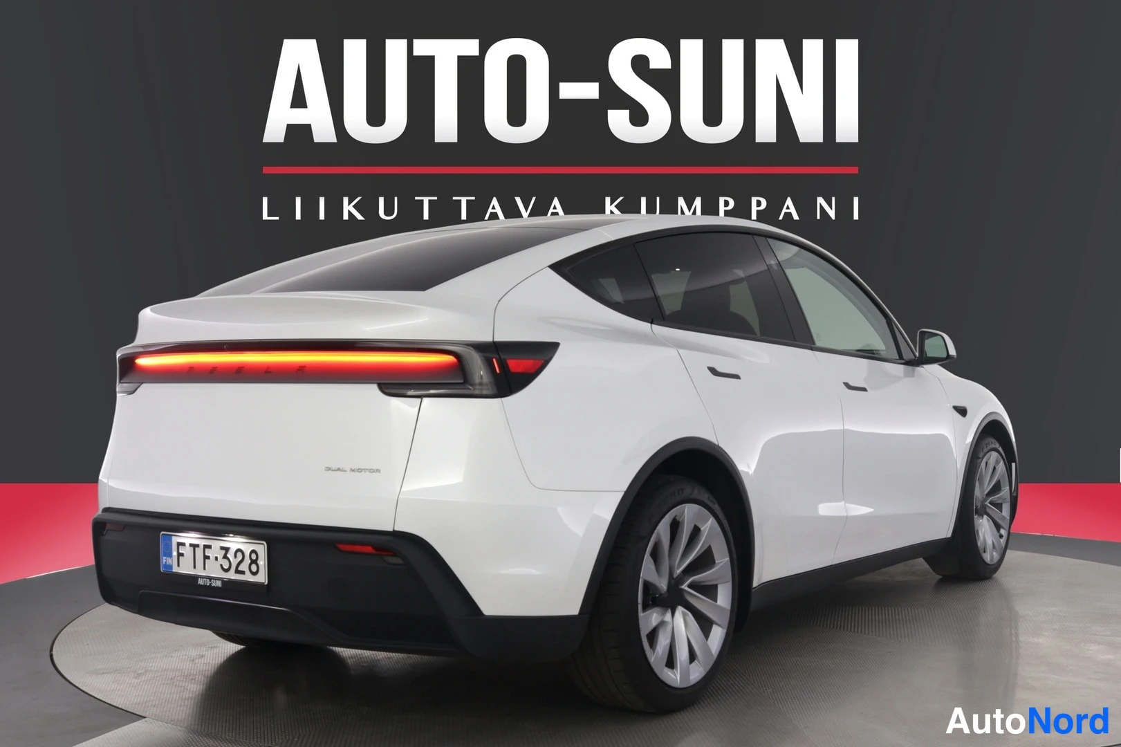 Takaviisto: Valkoinen Tesla Model Y takaa vasemmalta kolmesta neljäsosasta kuvattuna, punainen takavalotulin päällä.