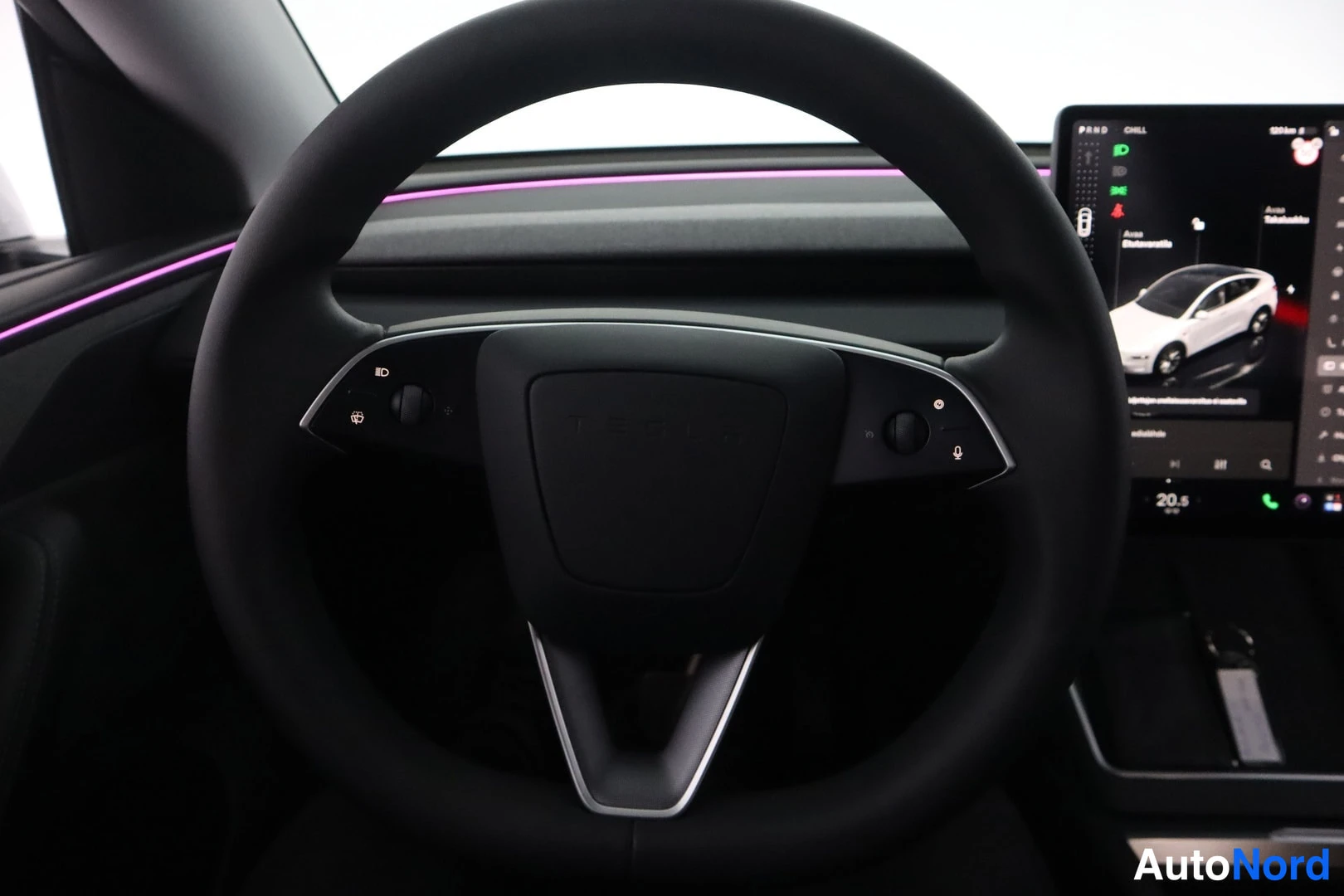 Muu: Tesla-merkkinen ohjauspyörä ja keskikonsolin kosketusnäyttö auton sisällä; näytössä P R N D -vaihdevalinnat ja valikko, kojelaudassa valaistuslista.