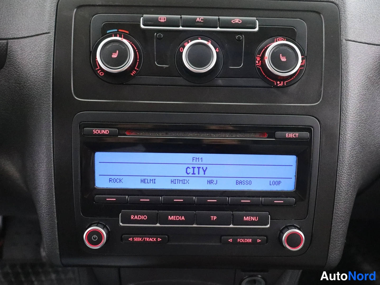 Takaa: Keskikonsolin aanuspaneeli: kolme säädinkiehura, lämpötilanäyttö, AC-nappi ja radio-näytöllä FM1 CITY.