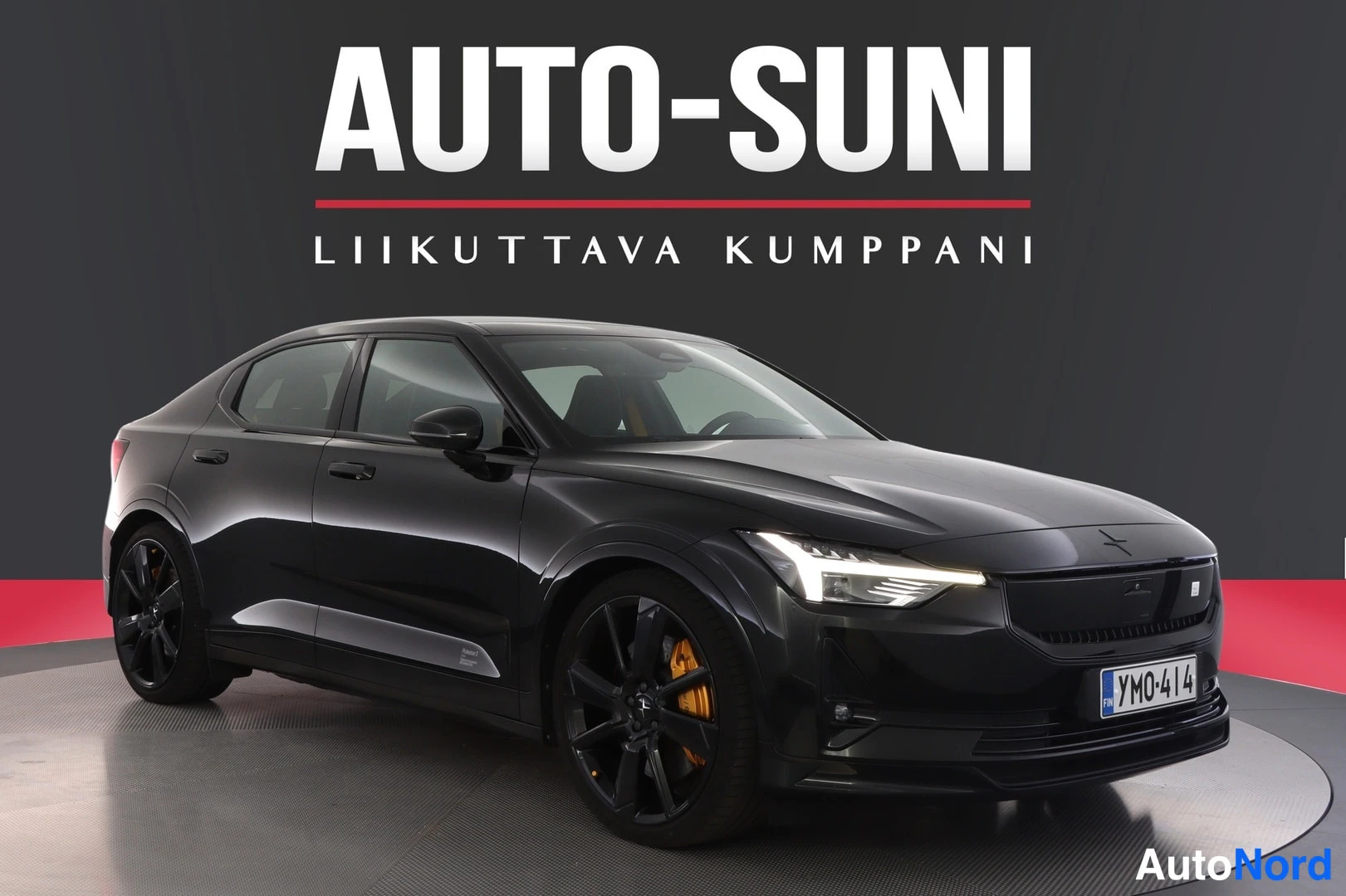 Etuviisto, nokka oikealle: Autosuni-studio: mustan sedanin etukulma, rekisteri, mustat kevytmetallivanteet ja oranssit jarrusatulat näkyvät.