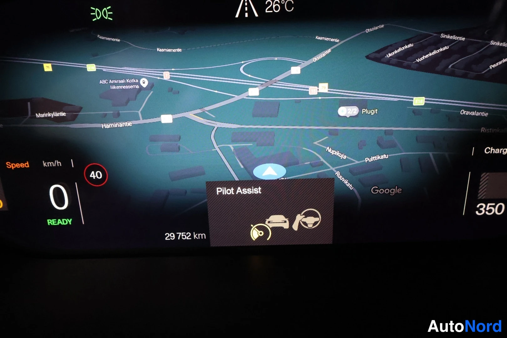 Yksityiskohta: Kojelautanäytön karttanäkymä, jossa Pilot Assist -ilmoitus, nopeus 0 km/h, READY-merkintä, lukema 29 752 km, ulkolämpötila 26 °C ja Google-kartta.