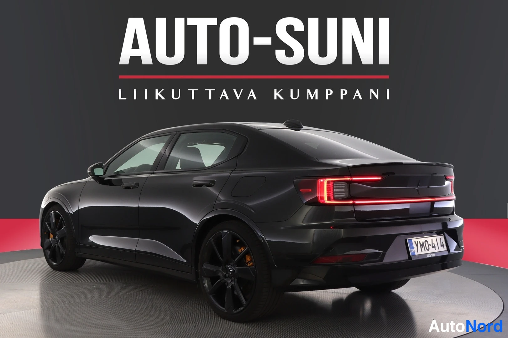 Takaviisto: Autosuni-studio: mustan sedanin takakulma vasemmalta, oranssi jarrusatula takapyörässä, rekisteri.