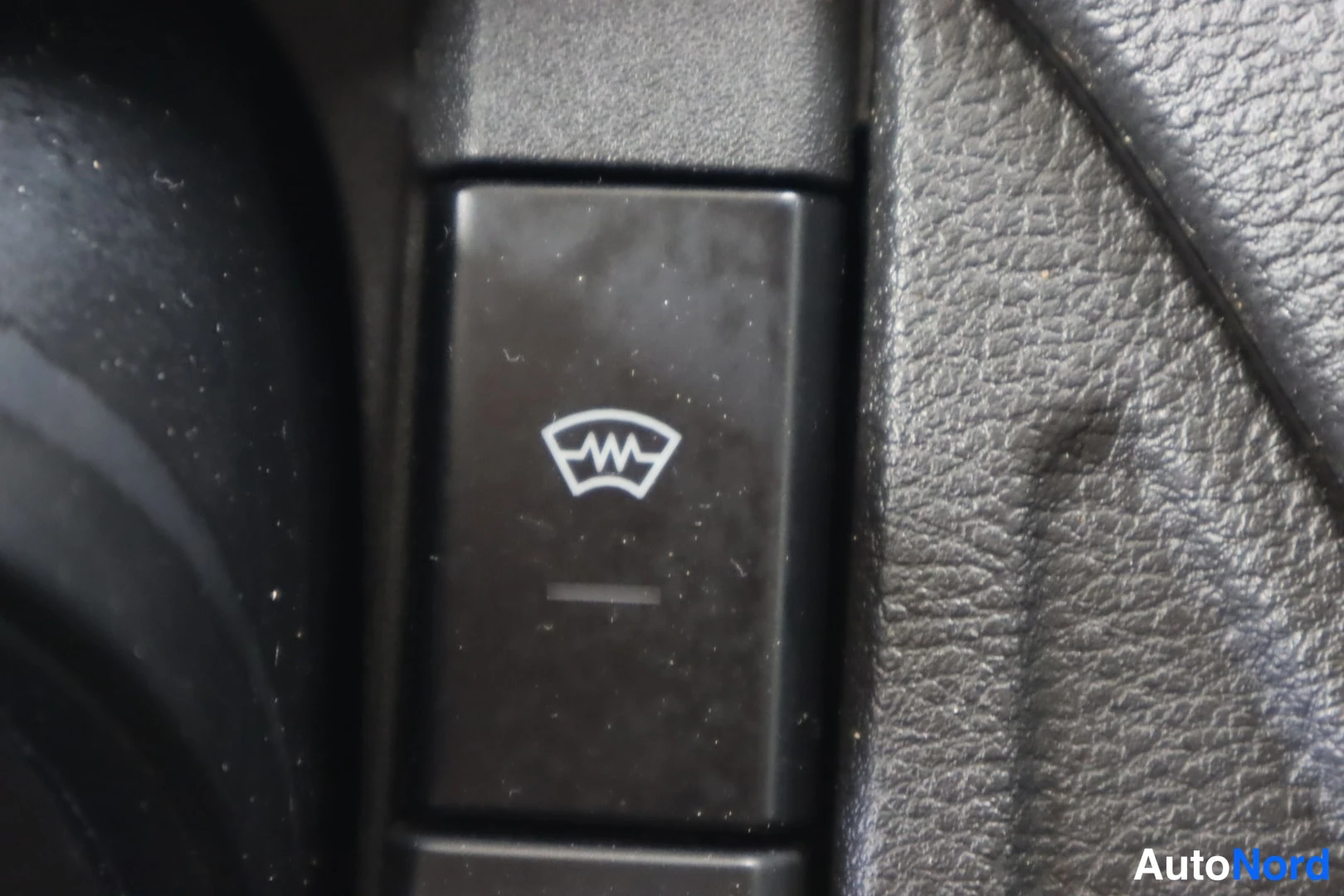 Yksityiskohta: Nearikuva auton kojelaudan napista, jossa on lämmitettävä tuulilasi -symboli.