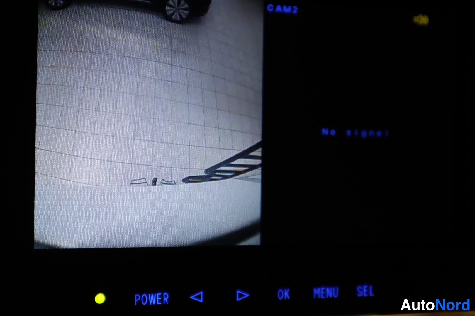 Yksityiskohta: Näytön kuva: kamerakuva katosta, teksti CAM2 ja No signal, alareunassa POWER-, OK-, MENU- ja SEL-painikkeet.