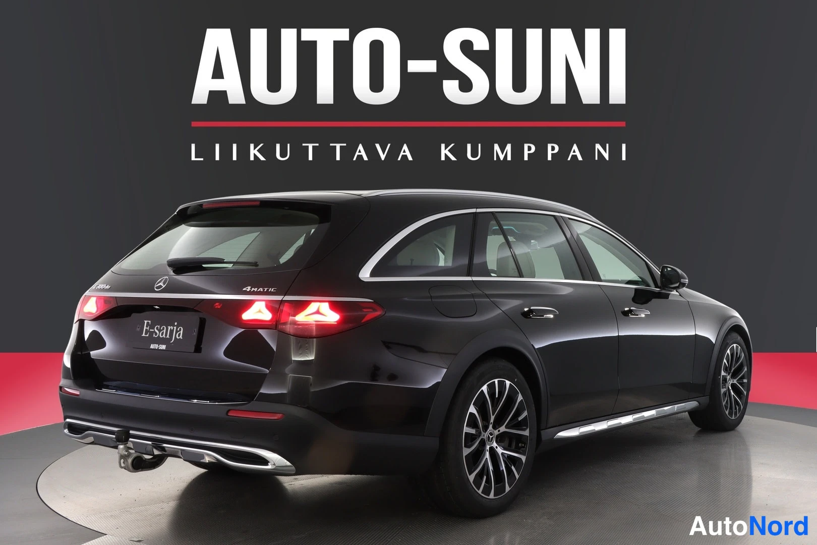 Takaviisto: Mustan Mercedes-Benz E -farmarin taka- ja sivukulma; takavalot ja vetokoukku näkyvät.