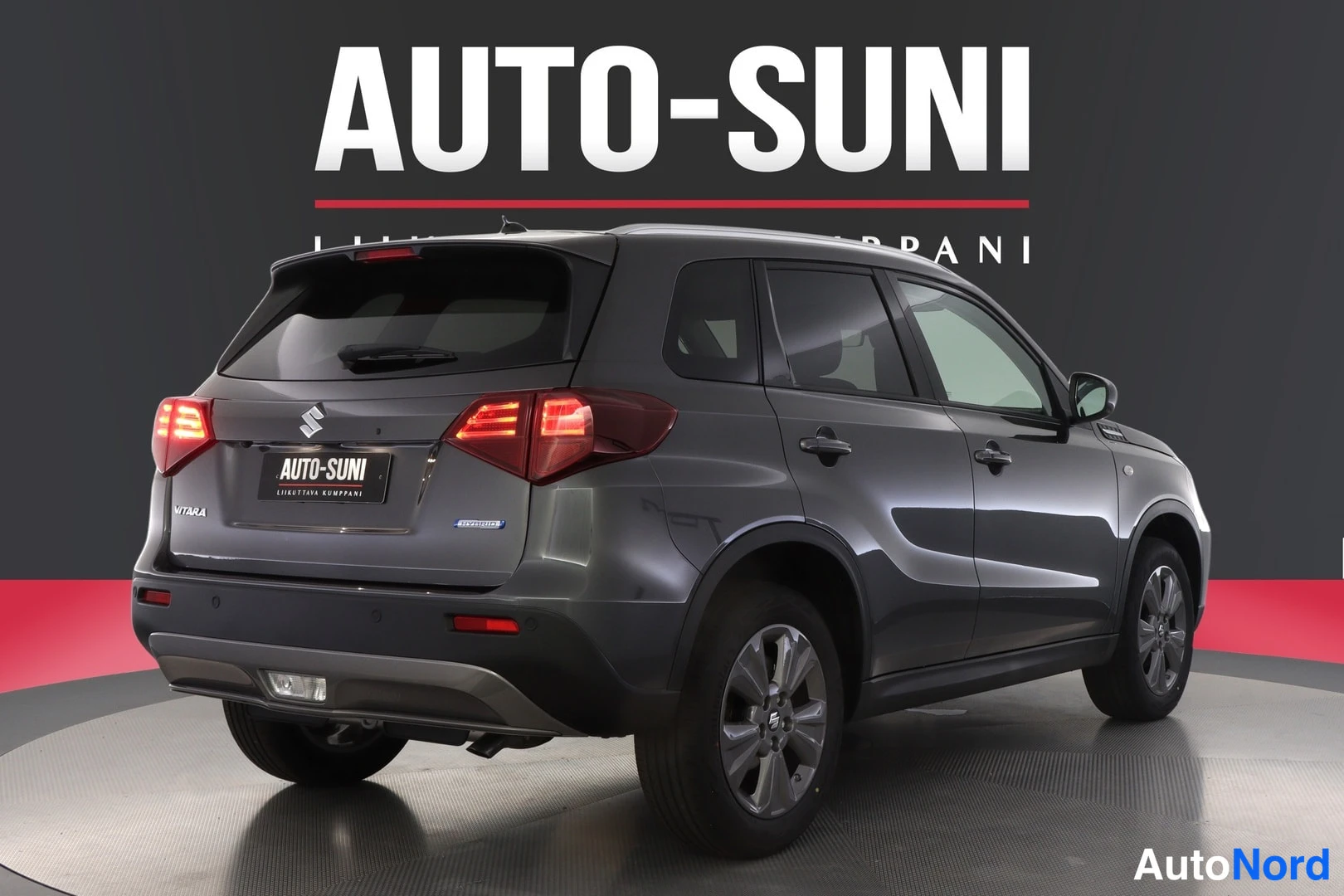 Takaviisto: Tummanharmaa Suzuki Vitara takaa kolmasosa-kulmasta, valaisimet palamassa studioympäristössä. Takaluukku, VITARA-kylki tai -teksti ja hopeiset kevytmetallivante