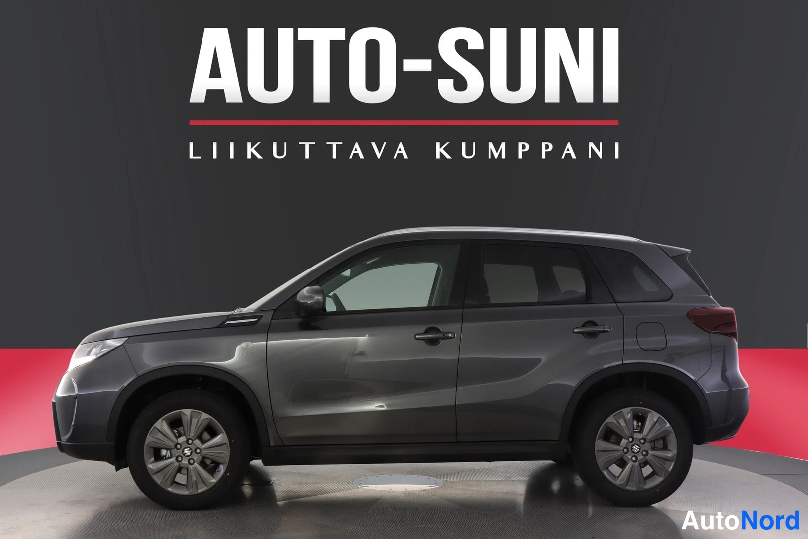 Etuviisto, nokka vasemmalle: Suzuki Vitara -asuma auton sivukulmassa, kokonaisuus harmaana studioseiniä vasten AUTO-SUNI-mainostekstillä