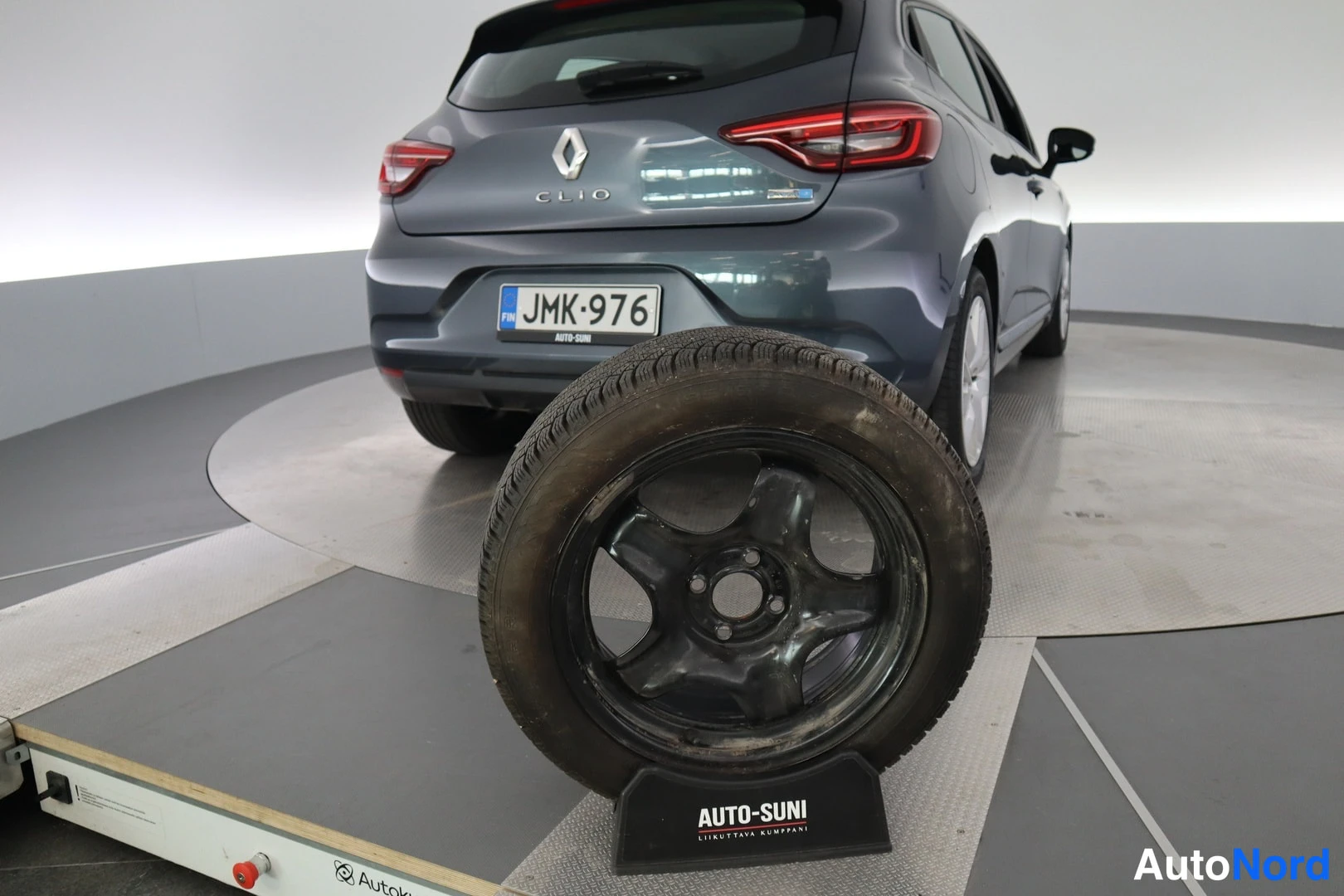 Takaviisto: Renault Clio auton takaosa näkyy -rekisterikilvellä; etualalla Auto-Suni-merkitty talvipyörä.