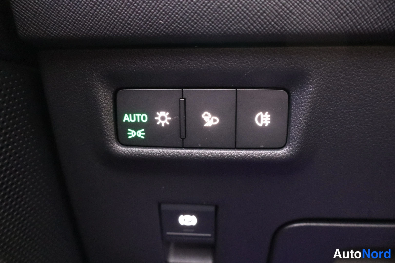 Muu: Autovalojenkytkinpaneeli sisäkatupanelissa; vasemman näppäimen AUTO-teksti ja valon symboli näkyvät vihreällä, keskellä sumuvalokytkin ja oikeassa etuvalokytkin