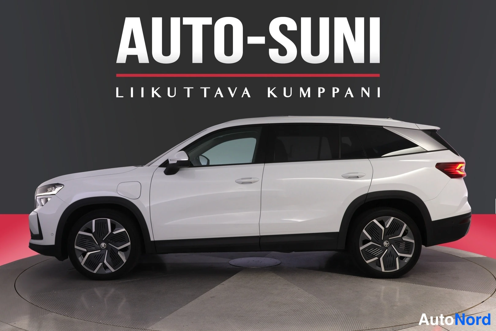 Etuviisto, nokka vasemmalle: Valkoinen Skoda Kodiaq -katumaasturin sivuprofiili studio­taustalla, AUTO-SUNI-teksti yläosassa.