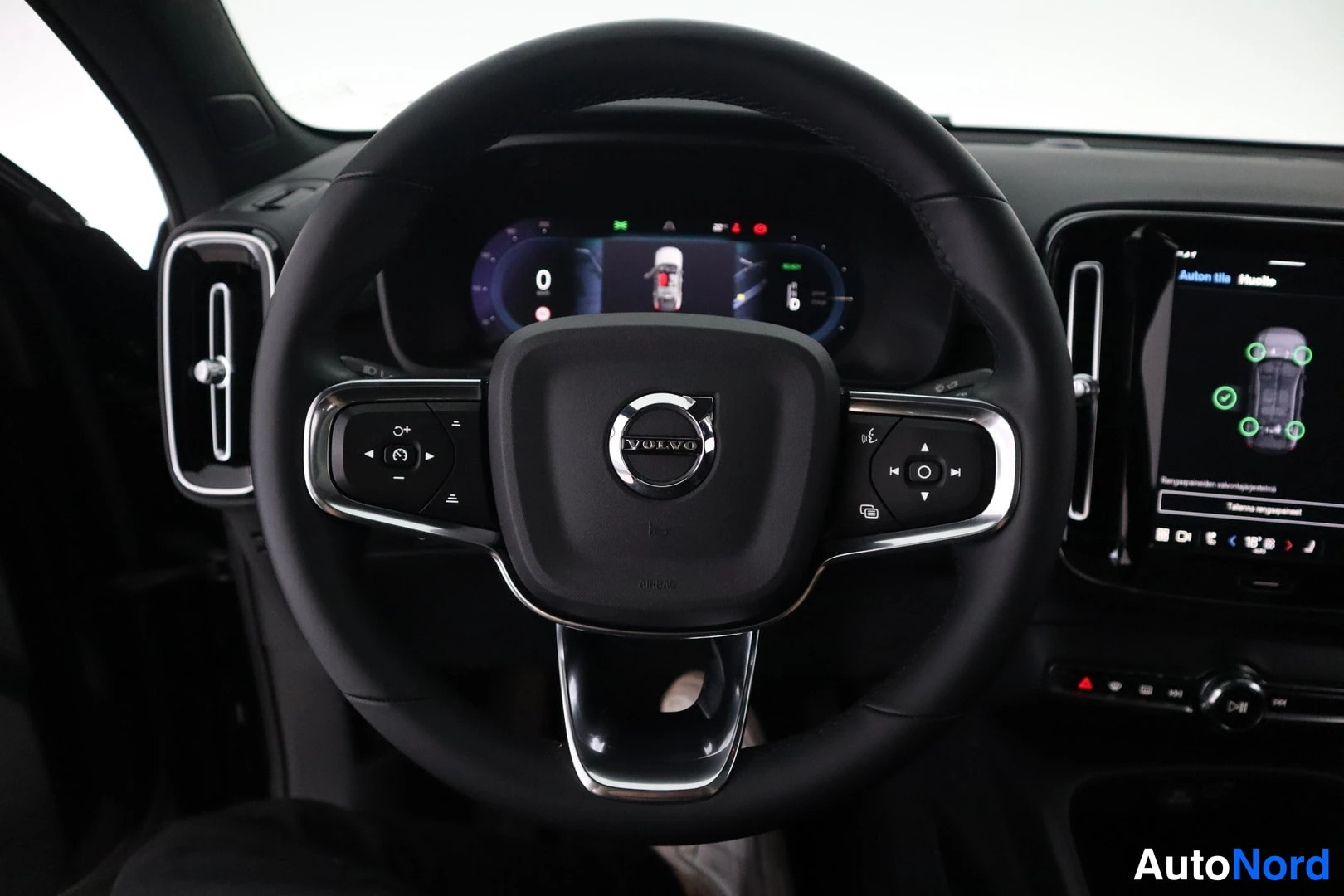 Takaa: Ohjauspyörän tarkennus: Volvo-logo, monitoiminäppäimet ja digitaalinen instrumenttinäyttö pysty-keskusnäytön vieressä.