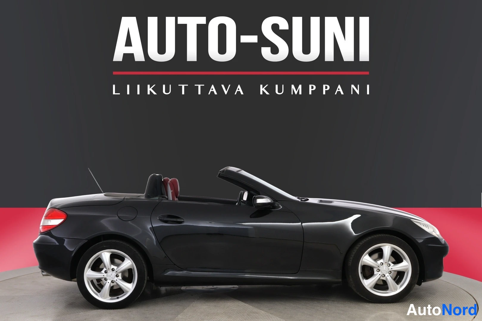 Sivulta: Mustan avoauton sivuprofiili, katto auki, punaiset istuimet osittain näkyvissä.