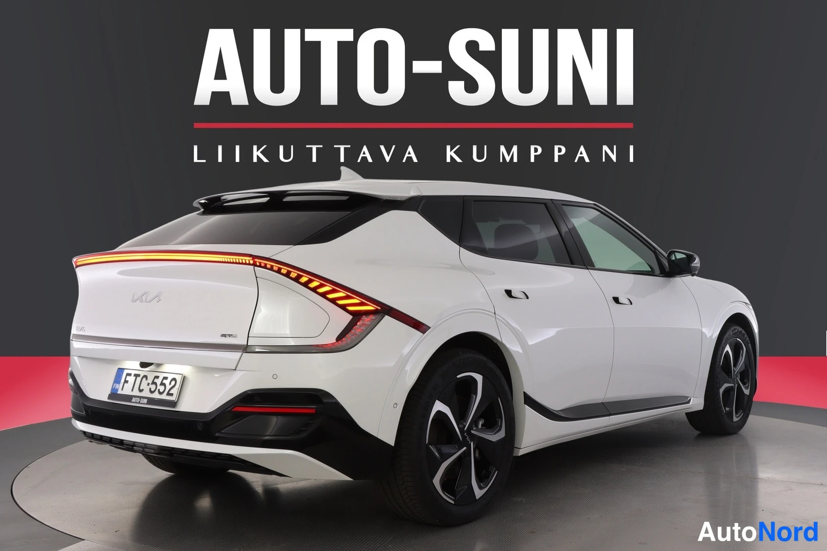 Takaviisto: Valkoinen Kia EV6 takakulmasta, takavalojen merkkivalot palavat oranssina, rekisterikilpi, musta studiosetausta.