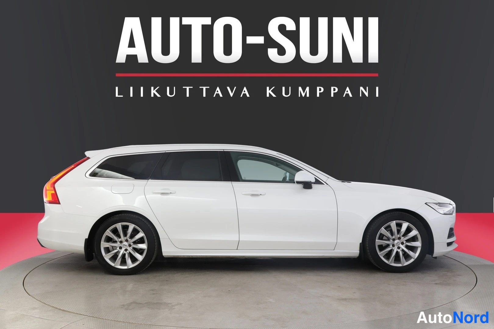 Sivulta: Koko valkoinen Volvo V90 kuvattuna oikeasta sivusta. Autossa on hopeiset kevytmetallivanteet ja valkoiset peilikotelot. Taustalla musta seinä ja AUTO-SUNI-logo.