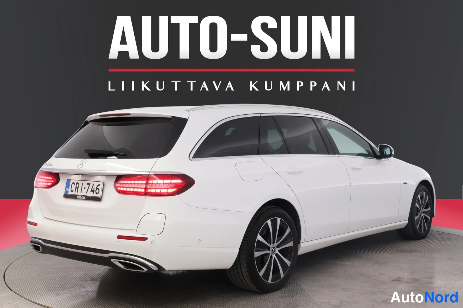Takaviisto: Valkoinen Mercedes-Benz farmari takaviistosta vasemmalle katsoen, rekisteri, takavilkut syttyneinä.