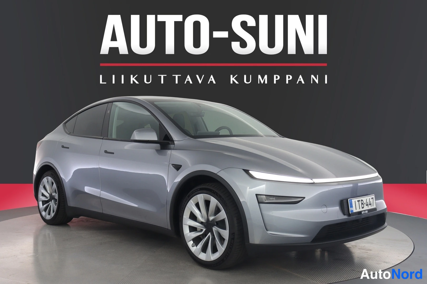 Etuviisto, nokka oikealle: Hopeanharmaa Tesla Model Y etukulmakuvassa myyntihallissa, rekisterikilpi