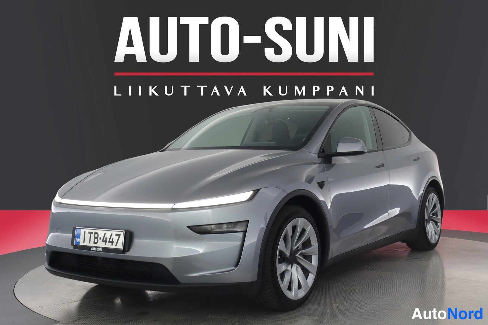 Etuviisto, nokka vasemmalle: Tesla Model Y, etupuoli ja vasen sivu kuvakulmasta, hopeanharmaa koriväri, rekisteritunnus, studiovaalea tausta.