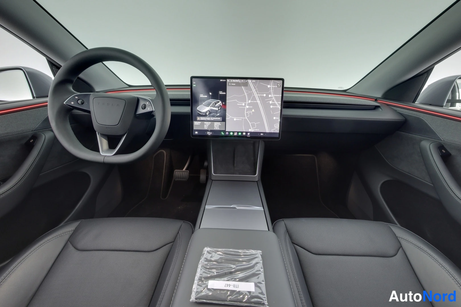 Muu: Tesla Model Y:n ohjaamo: keskikonsolin suuri karttanäyttö, ohjauspyörü ja etuistuimet tummassa sisustuksessa.