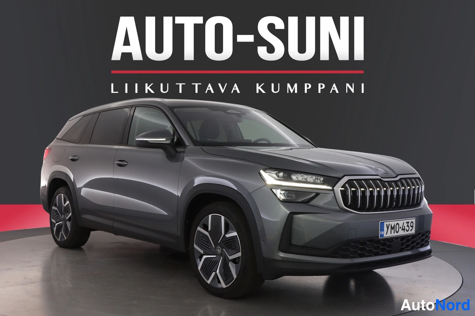 Etuviisto, nokka oikealle: Tummanharmaan Skoda Kodiaq -maasturin etukolmasosakuva studyyli-taustaa vasten, keulailme ja -rekisterikilpi näkyvät.