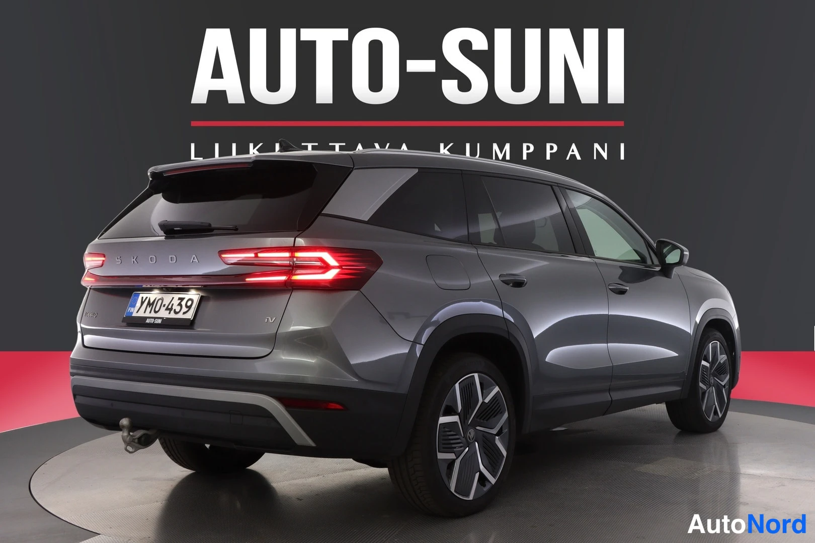 Takaviisto: Tummanharmaan Skoda Kodiaq -maasturin takakolmasosakuva studyyli-taustaa vasten, takavalot, -rekisterikilpi ja vetokoulu näkyvät.