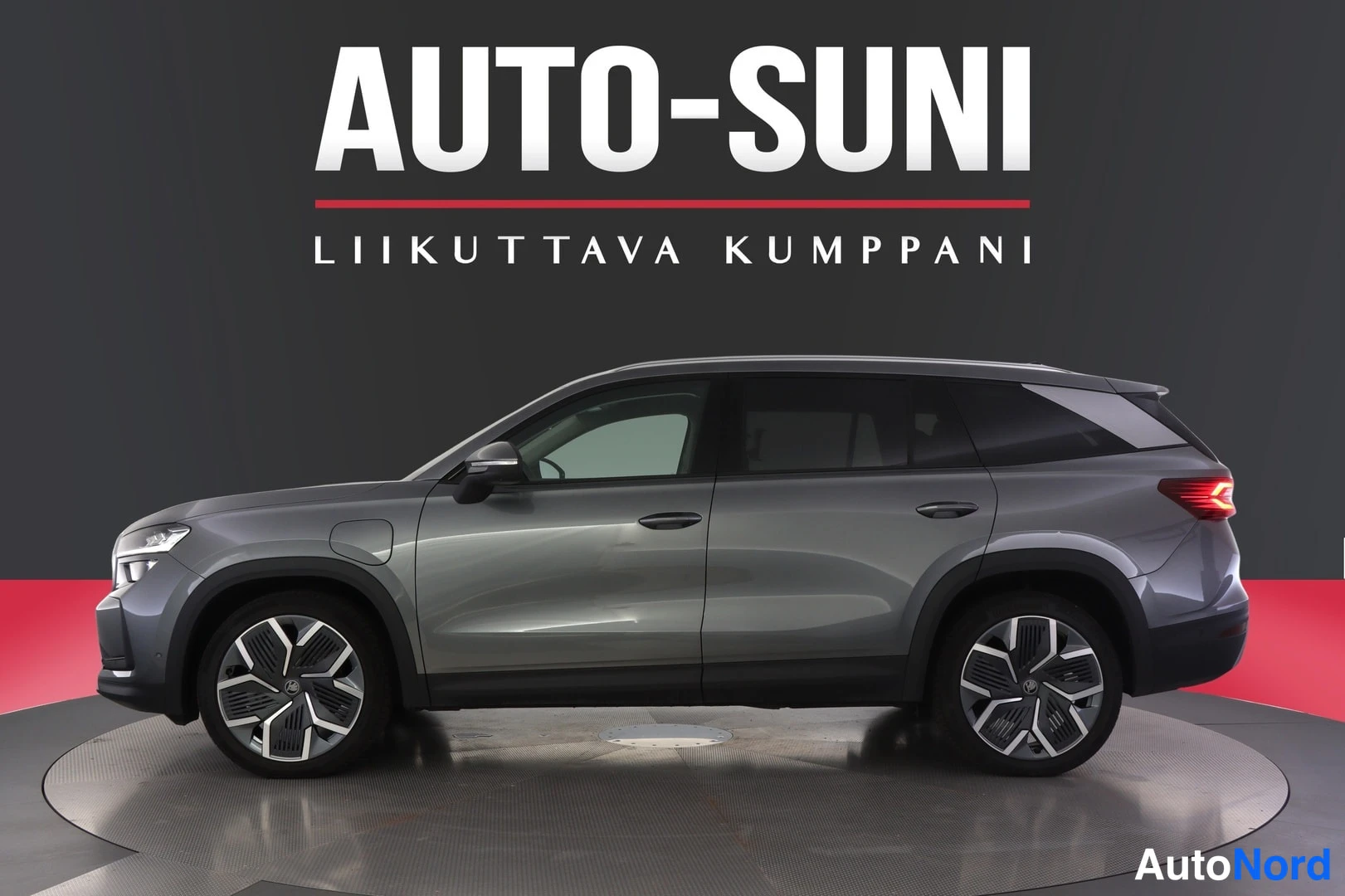 Sivulta: Skoda Kodiaq -maastokuva sivulta etukulmasta, harmaa kori, tummat ikkulat, dashboard mainostaulua vasten