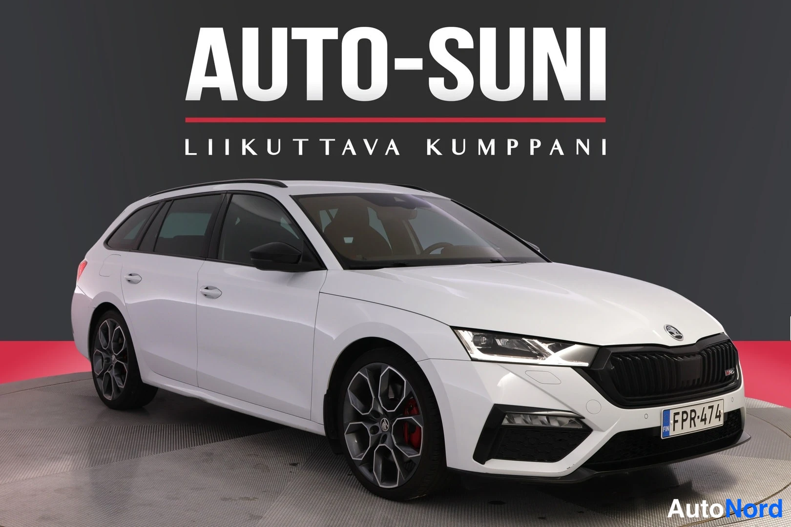 Etuviisto, nokka oikealle: Valkoinen farmariauto kolmelukon tehokkailla koneilla, etusivu vasemmassa yläkulmassa, taustalla musta pinta.