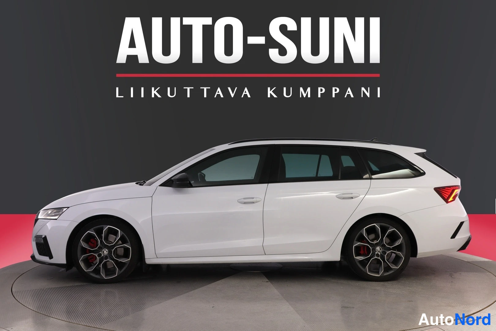 Sivulta: Valkoinen farmariauto sivulta etuosa vasemmalla, tummat vanteet ja punaiset jarrusatulat.