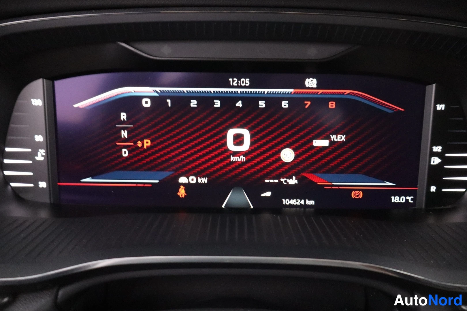 Muu: Digitaalinen mittaristo punaisella grafiikalla: nopeus 0 km/h, vaihteet R N D ja P, lukema 104624 km, kello 12:05, lämpötila 18,0 °C.